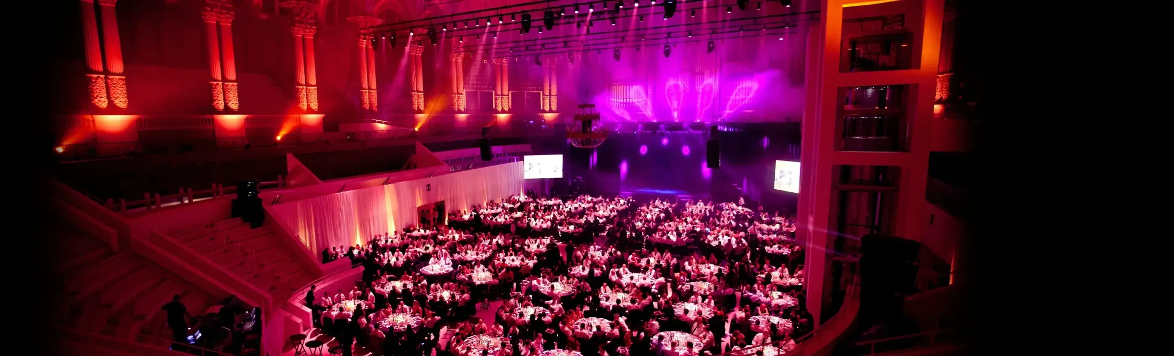 Panoramic view of a large corporate gala dinner with vibrant stage lighting