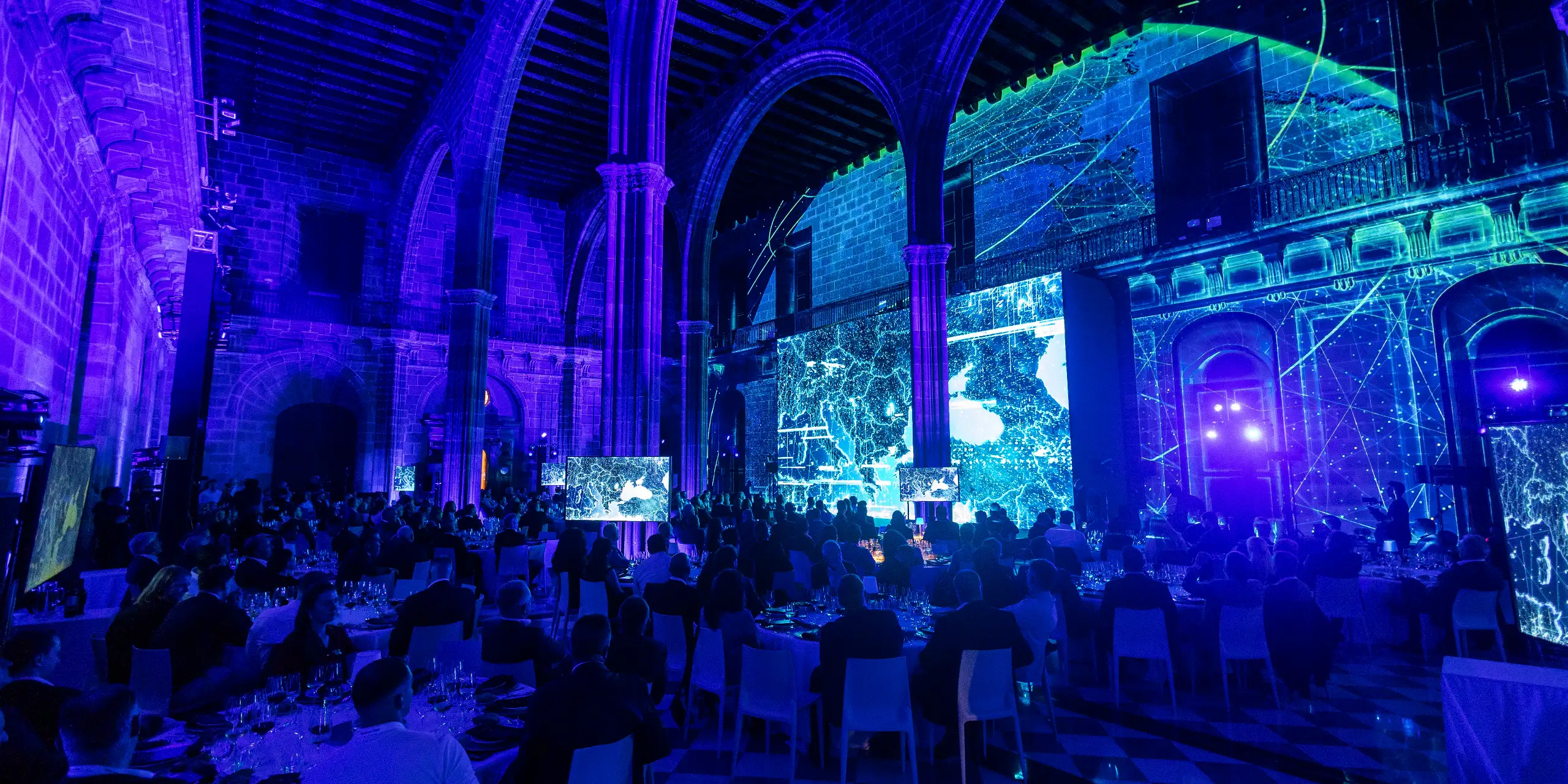 Gala dinner for a corporate group under Gothic stone arches, with immersive blue projection mapping and video screens